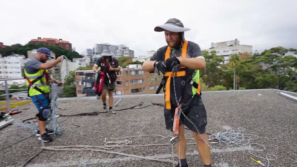 Roofers securing ropes and harnesses on a flat roof during a 24/7 emergency make-safe