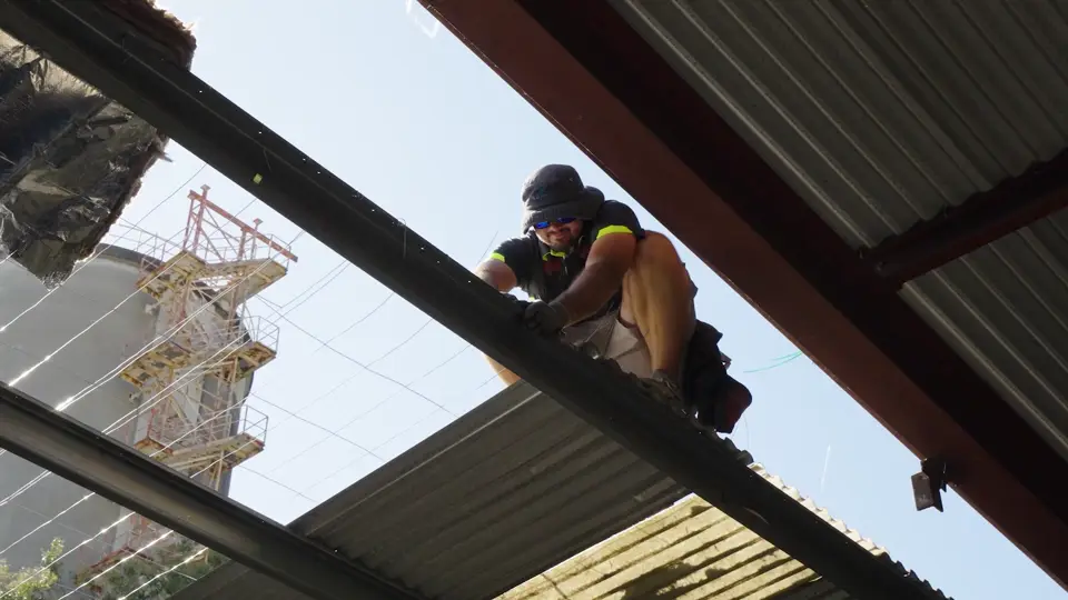 Roofer repairing corrugated metal roofing from the edge of the roof