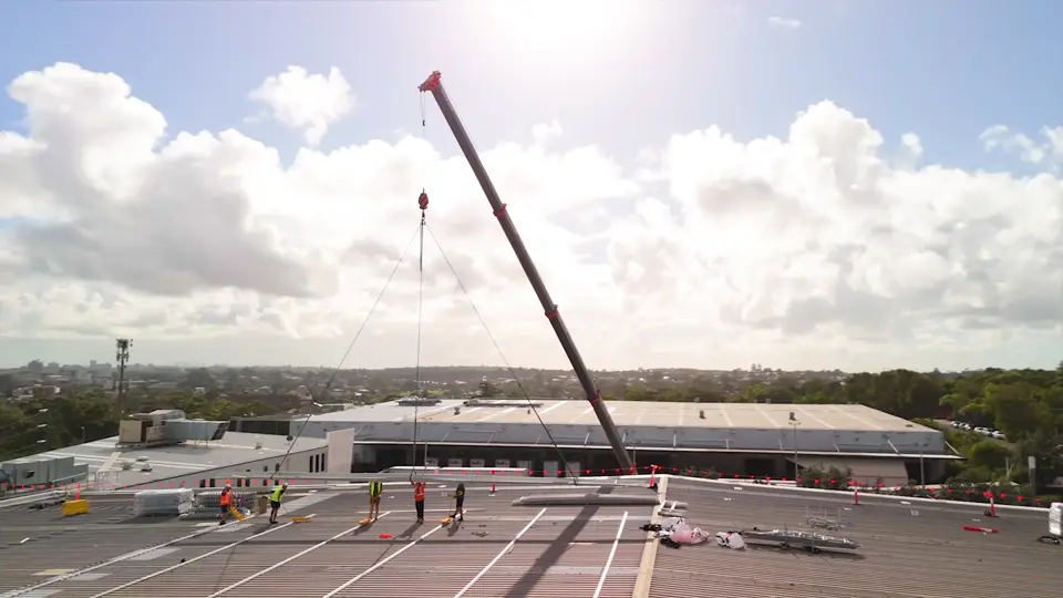 Crane lifting new roofing onto a commercial roof during a full roof replacement