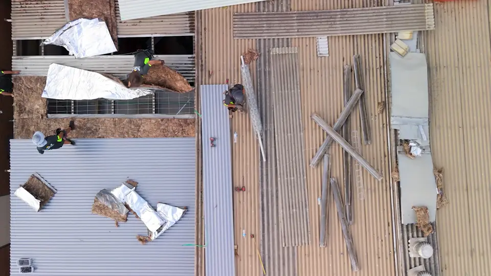 Aerial view of roofers restoring a metal roof, removing insulation and replacing sheets