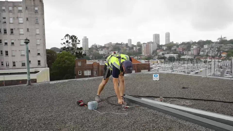 Roofer restoring ridge capping along a metal edge on a gravel roof above the harbour